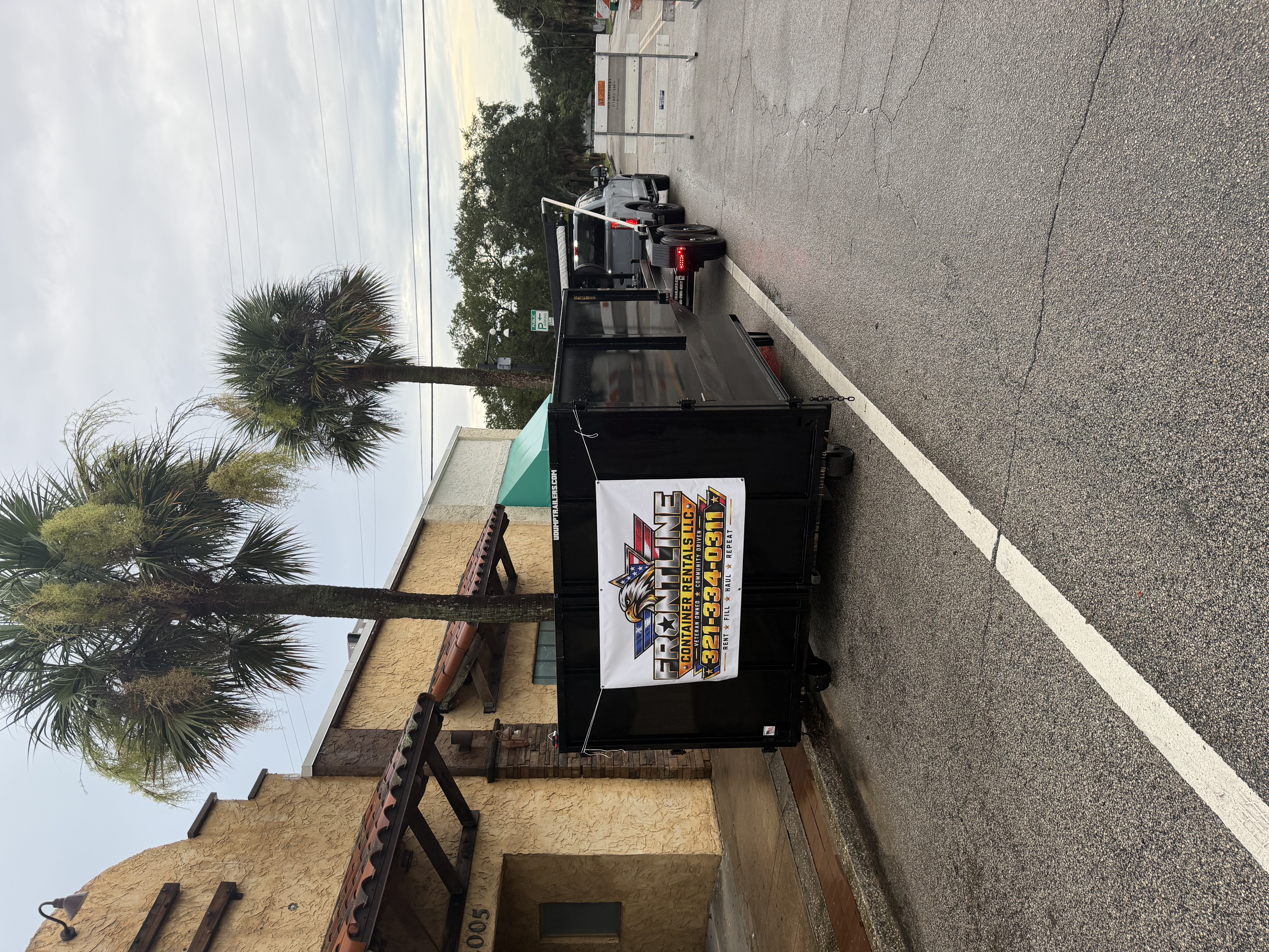 A black Frontline dumpster delivered outside a building, with the company logo and phone number visible on its banner.